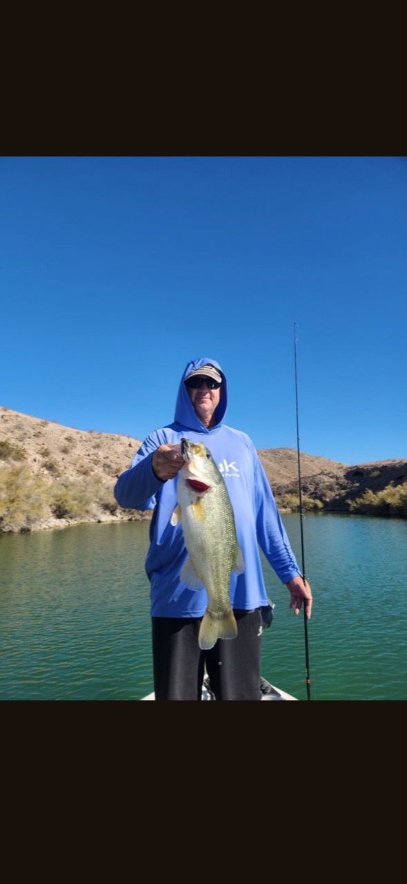 An angler in a blue hoodie holding a bass on the lake