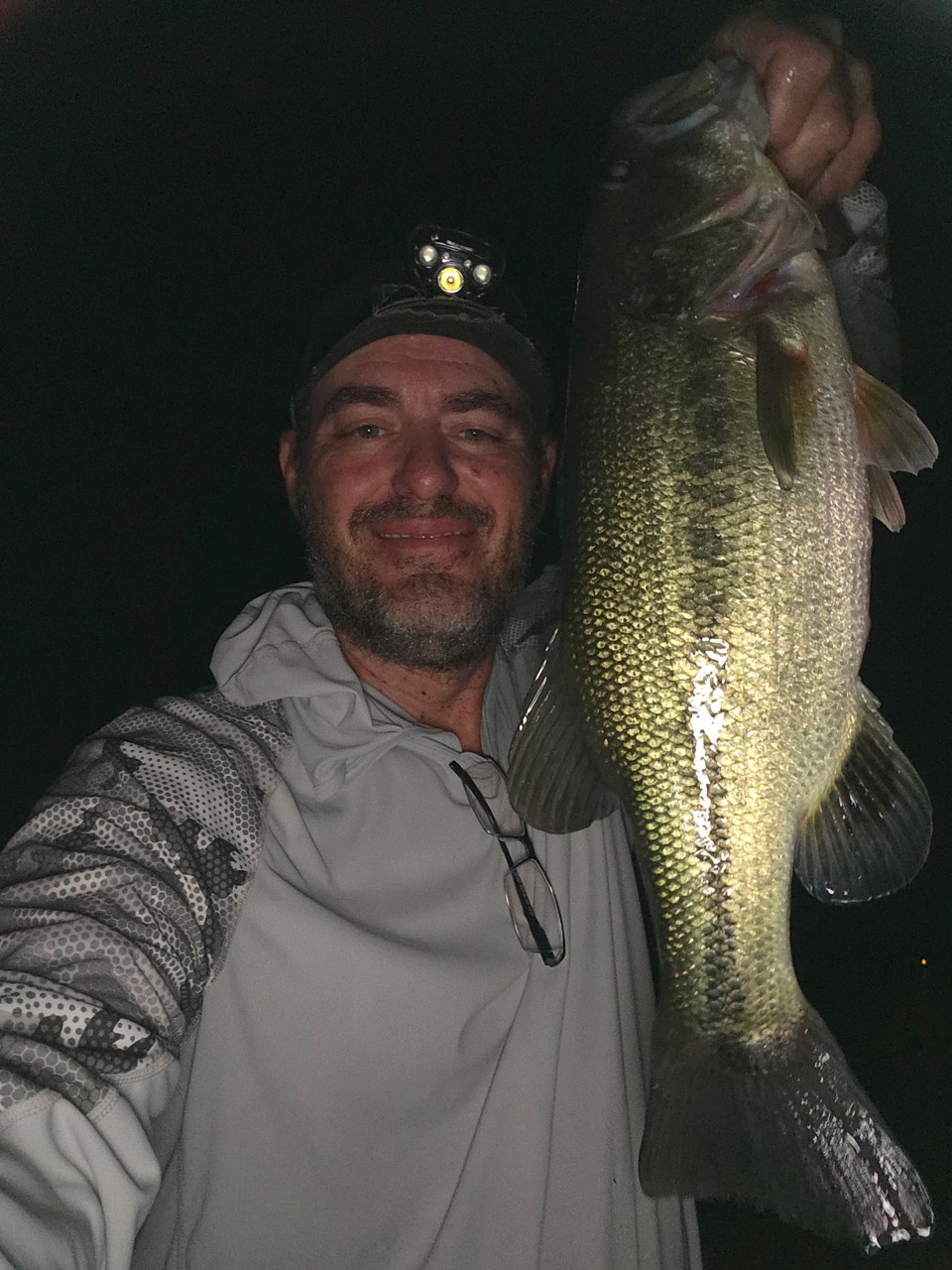 An angler wearing a headlamp holding a bass at night